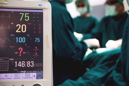 Surgeon at work. Surgery operating tool and heart rate monitor display with surgeons with his multi ethic team performing surgery on a patient in background. Real operating theater room. Medical concept.の写真素材