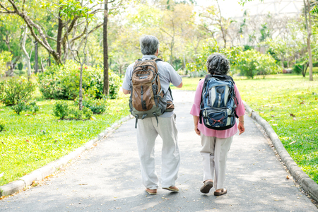 Senior couple in park walking with backpack. Chinese old couple in park, relaxing, smiling.の写真素材