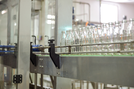 Beverage production line background. A conveyor belt full of empty glass bottle going into bottle filling machine. Beverage manufacturing concept.の写真素材