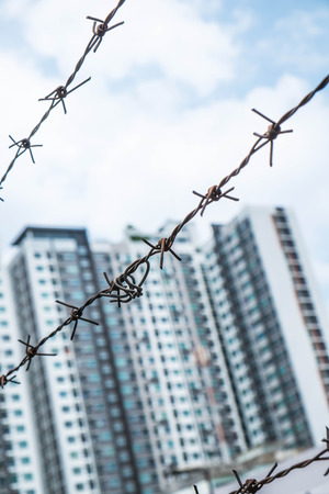 Shallow depth of field, old bared steel wire against blue sky with blurred modern buildingsの写真素材