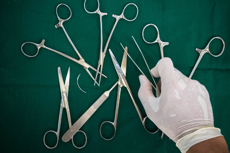 Hand holding forceps, with instruments for surgery