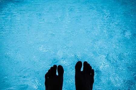 Silhouette feet on swimming pool water with shiny sunlight reflectionの写真素材
