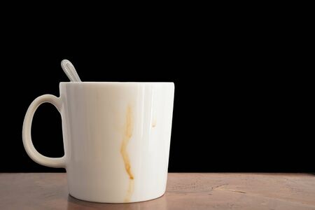 Cup of coffee with coffee stain on wood desk, isolated black background