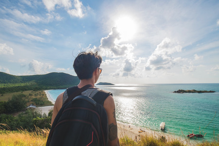 Asian guy with backpack standing on the mountain enjoying with ocean view on the islandの写真素材