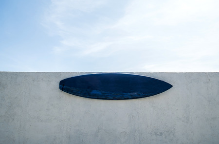 Surf board on white wall, and blue sky