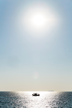 Silhouette fishing ship against the sun on the oceanの写真素材