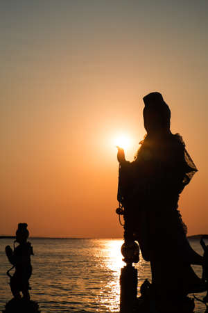 Silhouette, Goddess of Mercy Guan Yin, against the sun in sunsetの写真素材