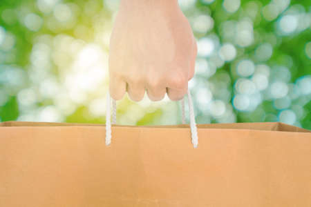 Hand holding reuse paper bag, on green Bokeh and bright yellow light backgroundの写真素材
