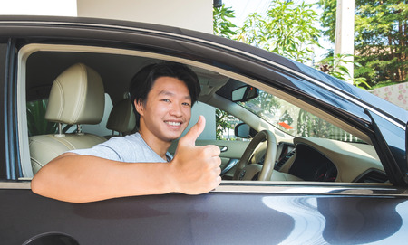 Asian man sitting in car, showing thumb up with smiling faceの写真素材