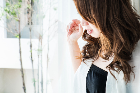 Asian girl look through window in the morning with smile face, selective focusの写真素材