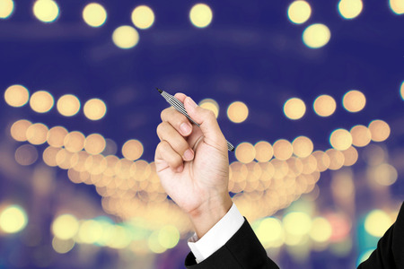 Businessman holding pen in writing position, with defocus Bokeh backgroundの写真素材
