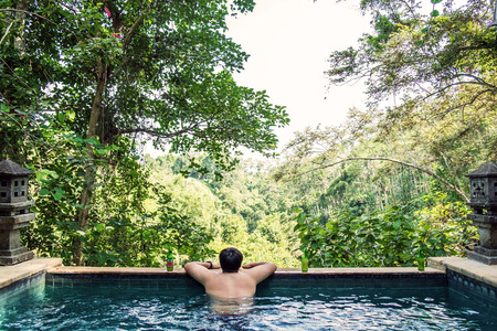 Rear view a guy relaxing in swimming pool in the forestの写真素材