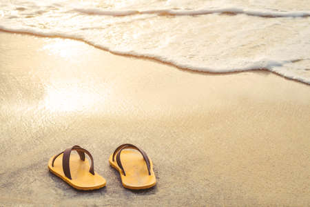 Yellow flip flop on the beach with bright light of sunset in summerの写真素材