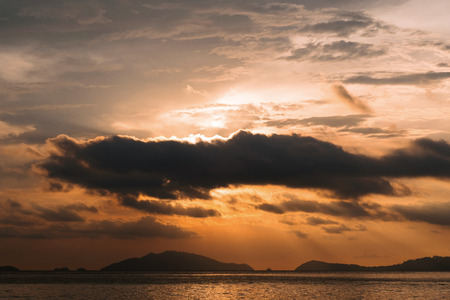 Sunset view on ocean in summer with sun behind cloudの写真素材