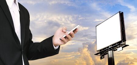 Businessman using smartphone with blank billboard for copy space on beautiful skyの写真素材