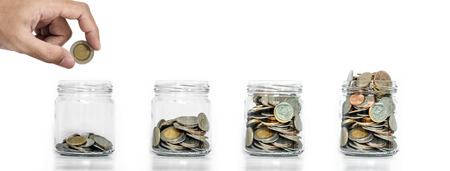 Money saving, Hand putting coin in glass jar with coins inside growing up, on white backgroundの写真素材