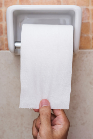 Close-up roll toilet paper in restroom with hand pullingの写真素材