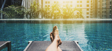 Relaxing in holidays, Asian guy feet on sun bathing bed at swimming pool in the cityの写真素材