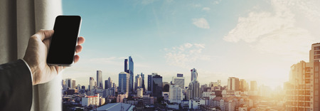 Hand holding mobile phone with panoramic cityscape of Bangkok city in sunrise, vintage toneの写真素材