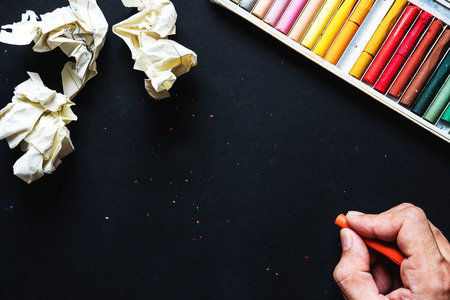 Hand hold orange crayon color, drawing on blackboard or black paper and crumpled paper ball, with copy spaceの写真素材