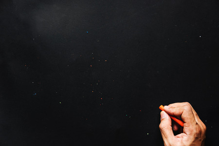 Hand hold orange crayon color, drawing on blackboard or black paper, and copy spaceの写真素材