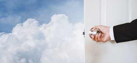 Businessman hand holding door knob, opening to the sky and clouds, with copy space, abstract business concept with copy spaceの写真素材
