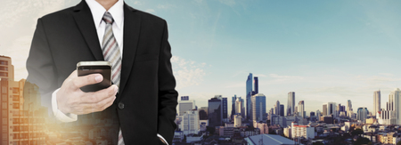 Businessman using mobile phone with panoramic cityscape of Bangkok city in sunriseの写真素材