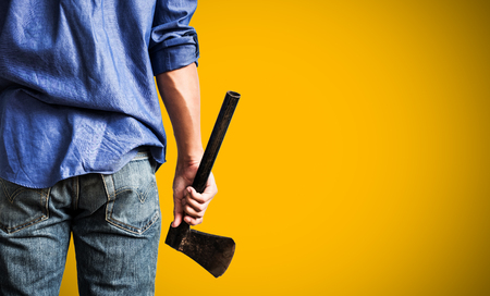 A guy holding old rusty axe, close up rear view, on yellow background with copy spaceの写真素材