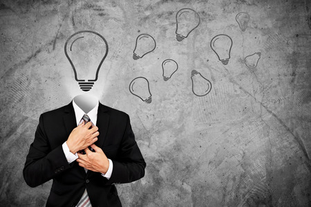 Businessman in black suit with light bulb instead head, on concrete background with copy spaceの写真素材