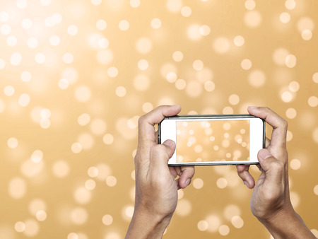 Hand using Smartphone taking a Photo of Defocus Gold Bokeh Lights Backgroundの写真素材