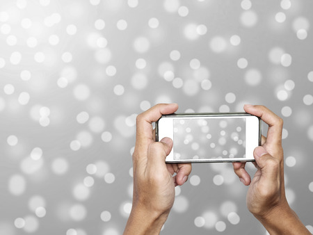 Hand using Smartphone taking a Photo of Defocus Snow Bokeh Lights Backgroundの写真素材
