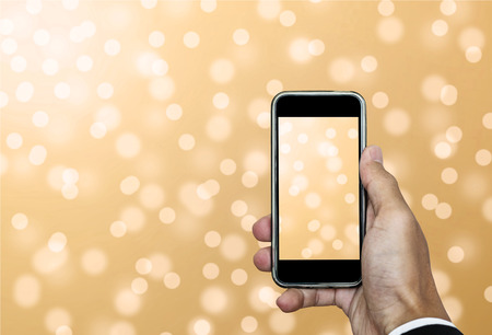 Hand using Smartphone taking a Photo of Defocus Gold Bokeh Lights Backgroundの写真素材