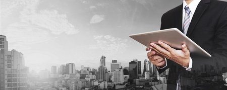 Businessman working on digital tablet outdoor, and city panoramic backgroundの写真素材