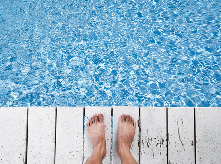 Naked foot on white wood panels at swimming pool, with water with sunlight reflection, holiday, relax, getaway conceptの写真素材