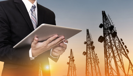 Businessman working on digital tablet, with satellite dish telecom network on telecommunication tower in sunset, telecommunication in business and developmentの写真素材
