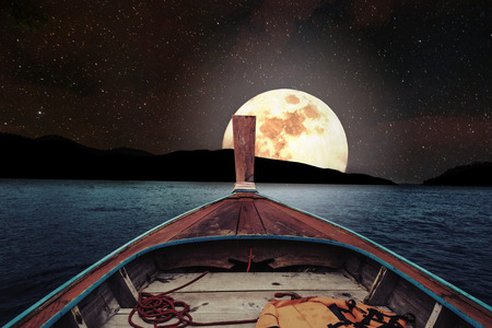 Traveling on wooden boat at night with full moon and stars on sky. romantic and scenic panorama with full moon on sea at nightの写真素材