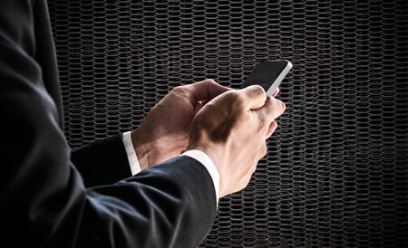 Businessman using smartphone, on blurred defocus black metal net backgroundの写真素材