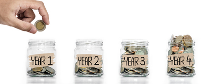 Money saving, Hand putting coin in glass jar with coins inside growing up, on white backgroundの写真素材