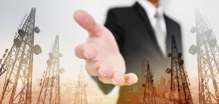 Businessman extending hand, with double exposure Telecommunication towers and city view in sunrise...