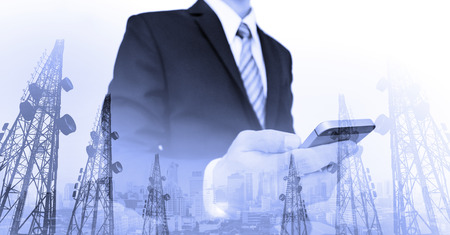 Businessman using smart phone with double exposure panoramic city and telecommunication towersの写真素材