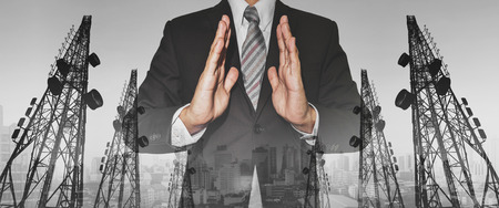 Businessman with panoramic double exposure telecommunication towers, and city in sunset backgroundの写真素材