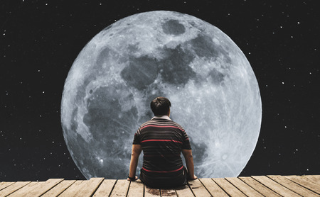 Silhouette a man sitting relaxing under full moon at night with stars on the skyの写真素材