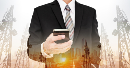 Businessman using smart phone with double exposure panoramic cityscape and telecommunication towersの写真素材
