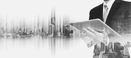 Businessman working on digital tablet with double exposure city, concepts of business communication technologyの写真素材