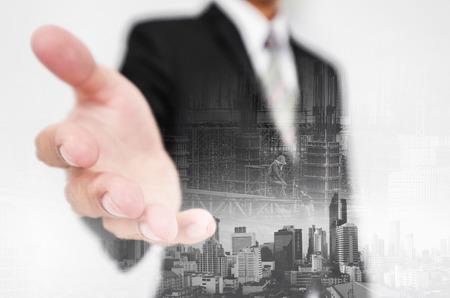 Businessman stretch out hand, with double exposure city and real estate site construction with workersの写真素材