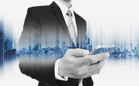 Businessman using smartphone, with double exposure city, business communication technology conceptsの写真素材