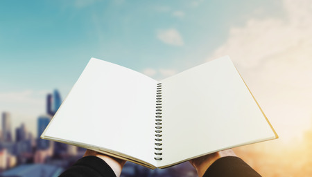 Opened book on hand with city backgrounds in sunriseの写真素材