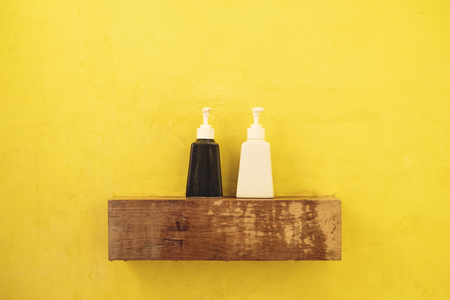 Black and white bottles container on wooden shelf in toilet with yellow wallの写真素材