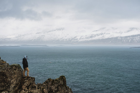 a man standing on cliff with the ocean and snow mountain viewの写真素材