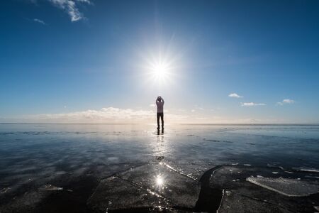 a man standing on frozen lake with sun and flare effects at winterの写真素材